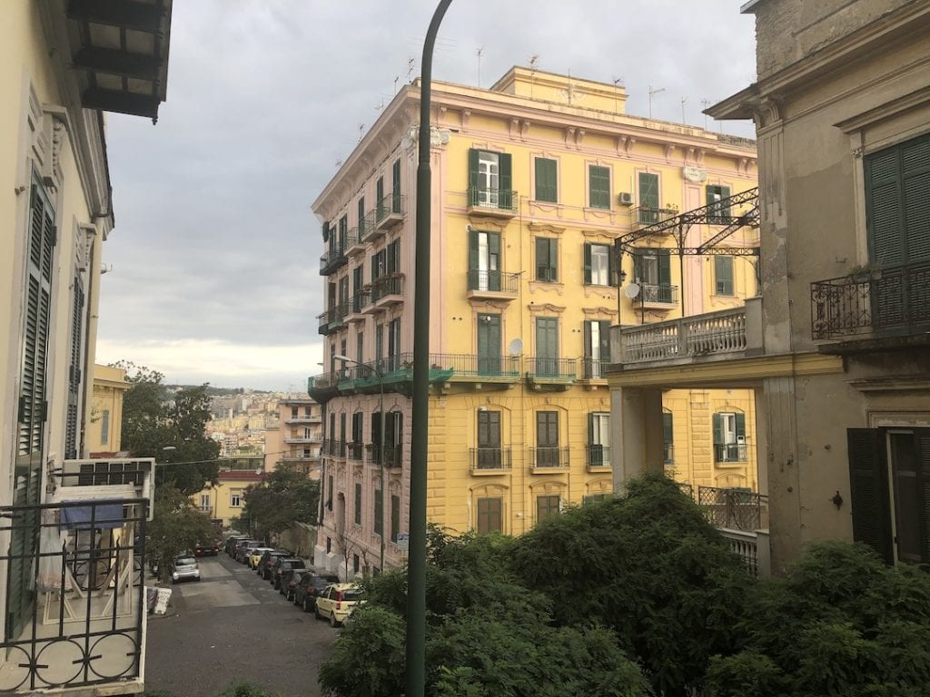 Colourful European city street with vibrant pastel buildings, lush greenery, and parked cars, capturing the charming architecture and lively atmosphere perfect for travel and exploration content.