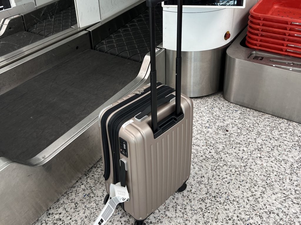 Compact beige Level8 Grace carry-on suitcase with telescopic handle and wheels, ready for travel at airport check-in counter.
