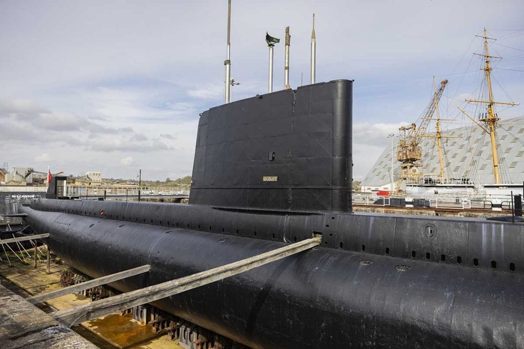 Submarine docked at the harbour with a visible conning tower and hull, part of a maritime museum or naval base in the east of England, UK.