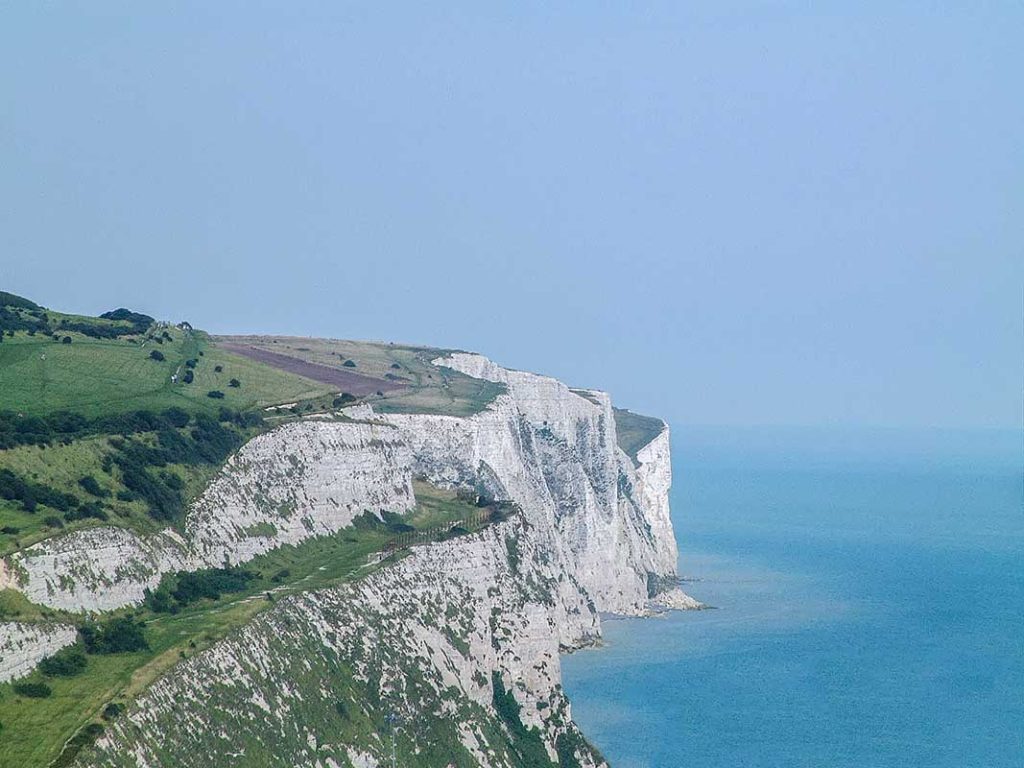 Stunning white chalk cliffs along the east coast of England, part of a scenic road trip route. The cliffs overlook the North Sea, with lush green fields at the top.