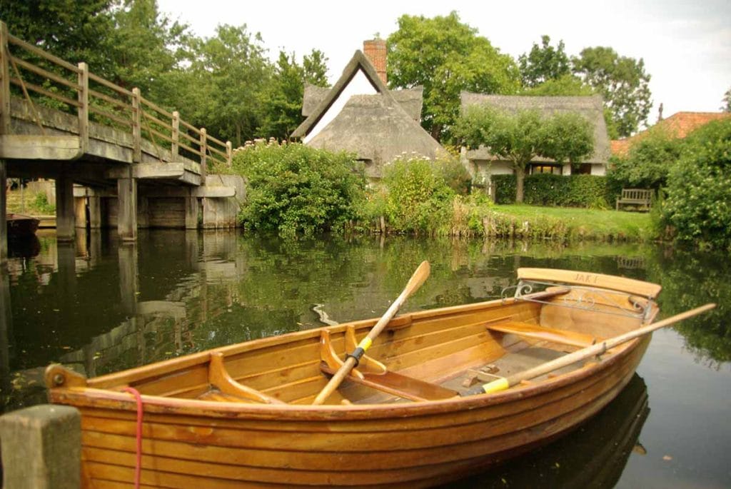 A traditional wooden boat floating on a peaceful river in the East of England, surrounded by lush greenery and historic cottages, perfect for exploring scenic waterways.