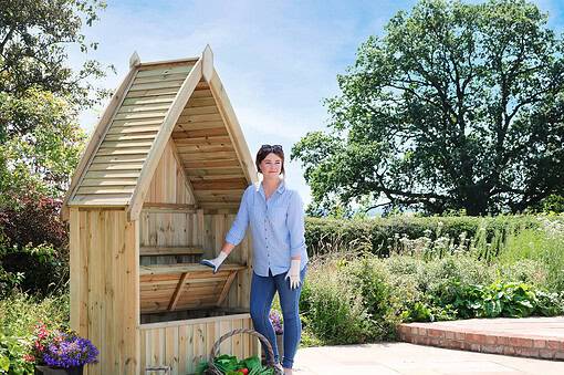 Wooden garden shed under construction in a lush outdoor garden setting.