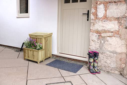 Bright front door entrance with a cozy outdoor decor, wooden planter with colorful flowers, and floral rain boots, showcasing stylish home and garden design elements.