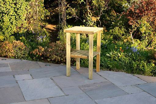 Rustic wooden outdoor garden side table in a lush landscaped backyard with colorful plants and flowers, ideal for garden decor and outdoor entertaining.