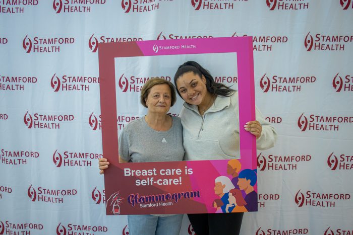 Two women hold a poster during Stamford Health's "glammogram" initiative. 