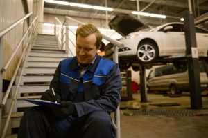 young-caucasian-auto-mechanic-sitting-stairs-repair-shop-writing-checklists-clipboard-inspecting-car-workshop-mechanical-maintenance-engineer-working-automotive-industry