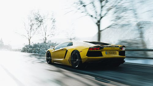 Yellow sports car driving on snow-covered road during winter.
