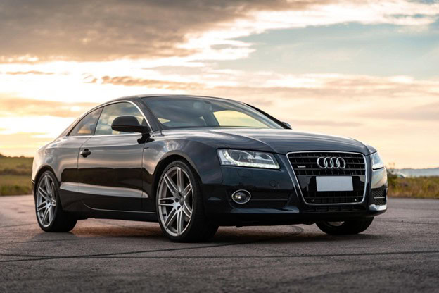 Black Audi coupe on open road at sunset, showcasing premium vehicle restoration.