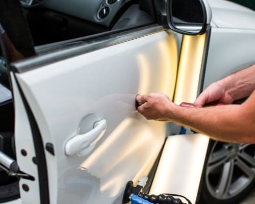 Skilled technician performing paintless dent repair on car door.