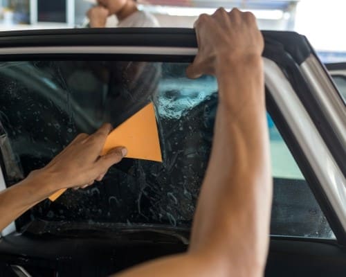 Technician replacing car windshield at European Autoworks auto body shop.