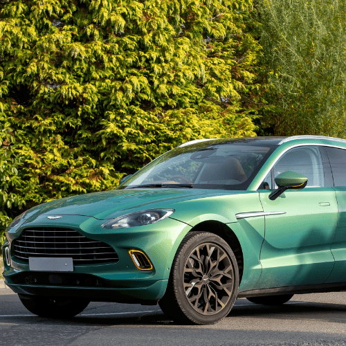 Modern green luxury car parked outdoors with trees in background.