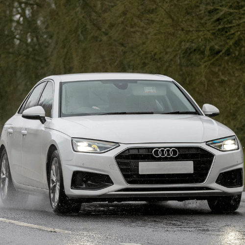 White Audi sedan driving on wet road, vehicle servicing by European Autoworks.