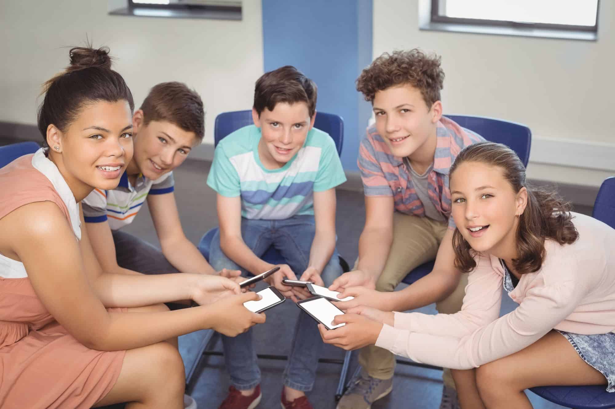 a group of kids sitting in a circle holding smartphones