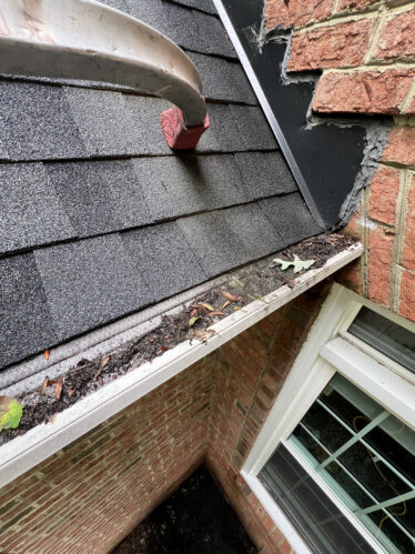 Close-up of a dirty gutter filled with leaves and debris on a brick house in Cincinnati, KY.