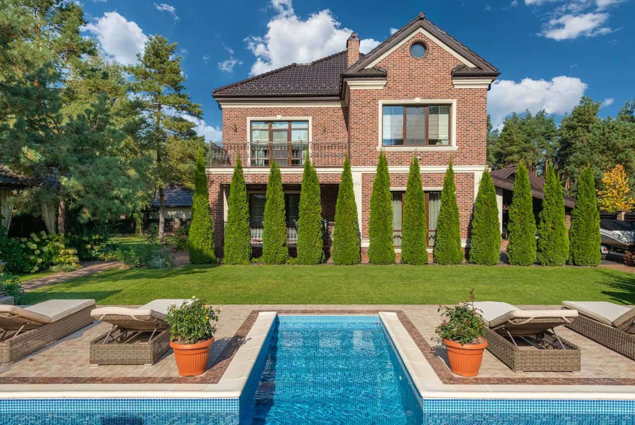 who-we-are Facade of brick dwell villa with green bushes on lawn and sunbeds near swimming pool