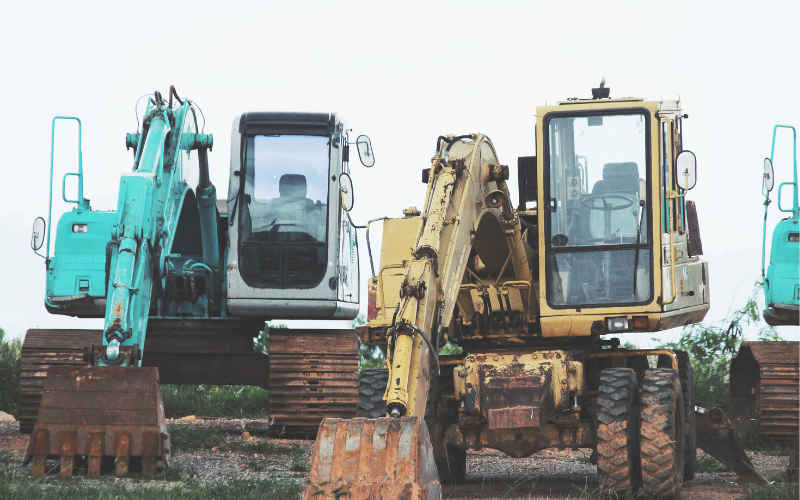 Backhoe vs. Wheel Loader: A backhoe with a front loader bucket and rear digging arm next to a wheel loader with a large front bucket, highlighting their different designs and functions