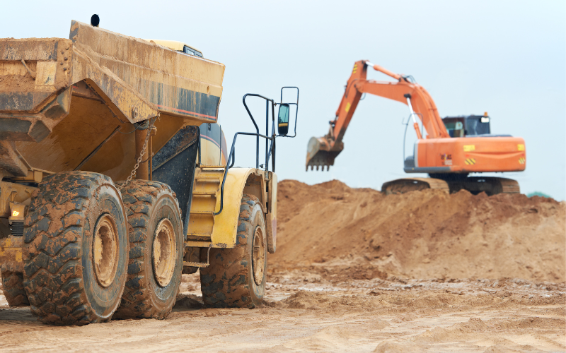 Backhoe vs. Wheel Loader: Two construction machines side by side, a backhoe with a front bucket and rear digging arm next to a wheel loader with a large front bucket, illustrating the choice between versatility and material handling
