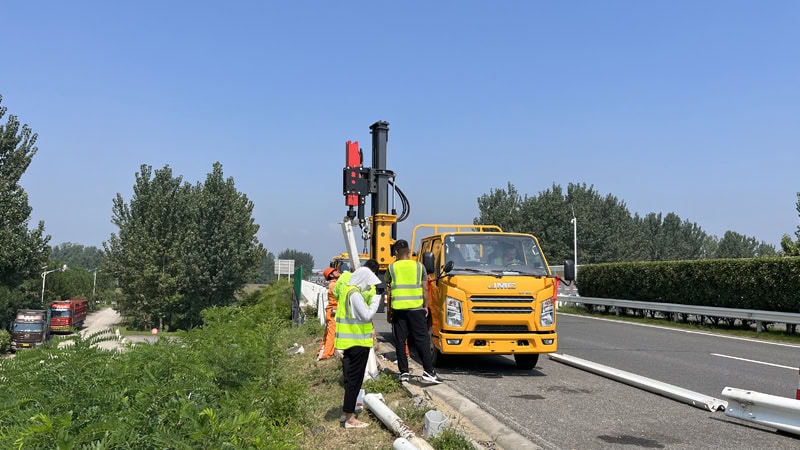 A truck-mounted pile driver is repairing the highway guardrail.