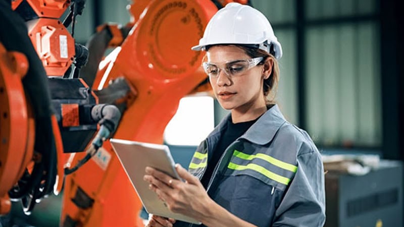 An engineer wearing PPE checks data next to a machine