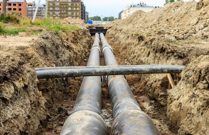 Black pipes installed in a muddy trench at a construction site.