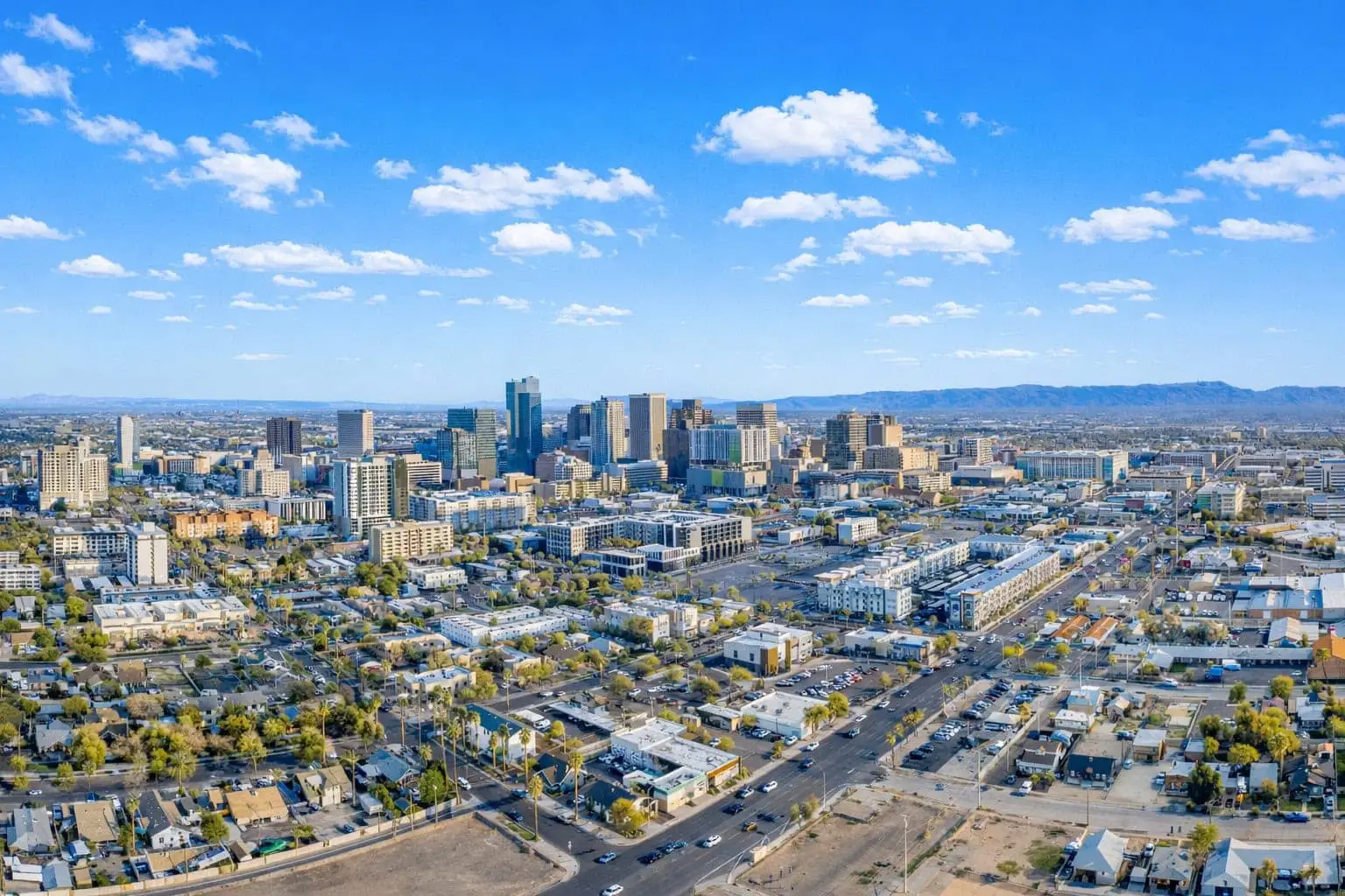 Aerial view of a vibrant city with skyscrapers, residential areas, and busy streets under a bright sky.