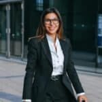 Businesswoman in formal attire smiling outside modern office building.