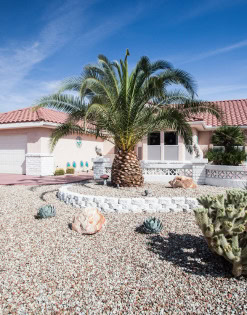 Beautiful desert home with a large palm tree and desert landscaping in front.