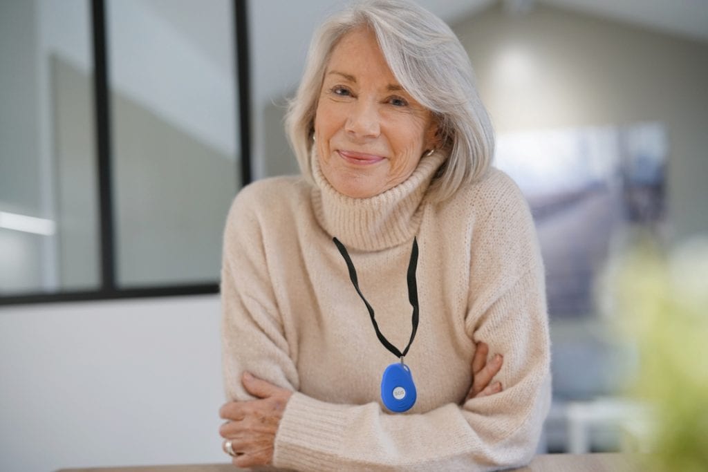 Senior woman wearing a medical alert device around her neck indoors.