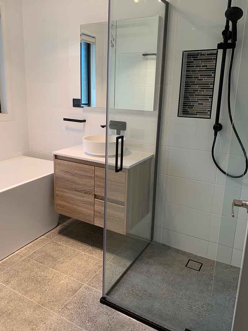 Glass shower with black fixtures and a wooden vanity.
