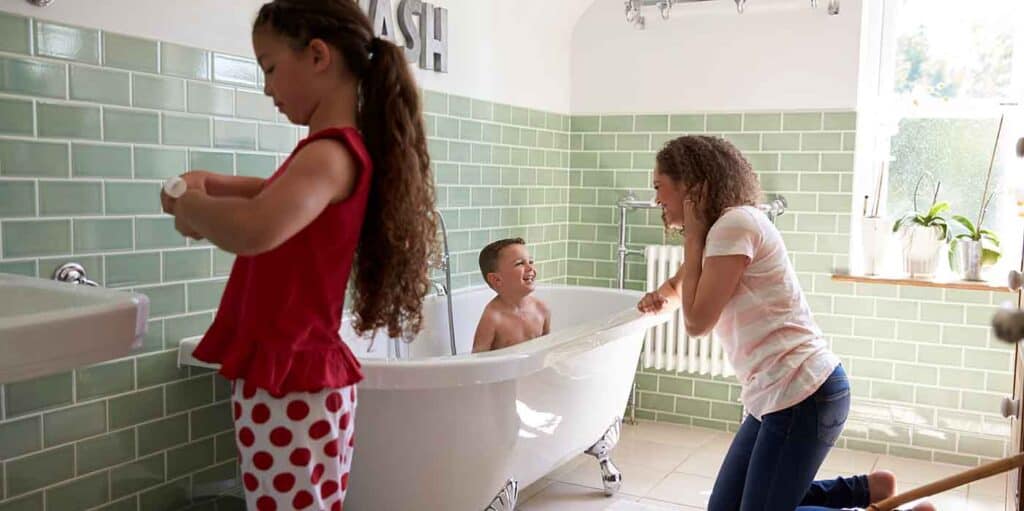 Kids enjoying bath time in a child-friendly bathroom with green tiles and natural light.