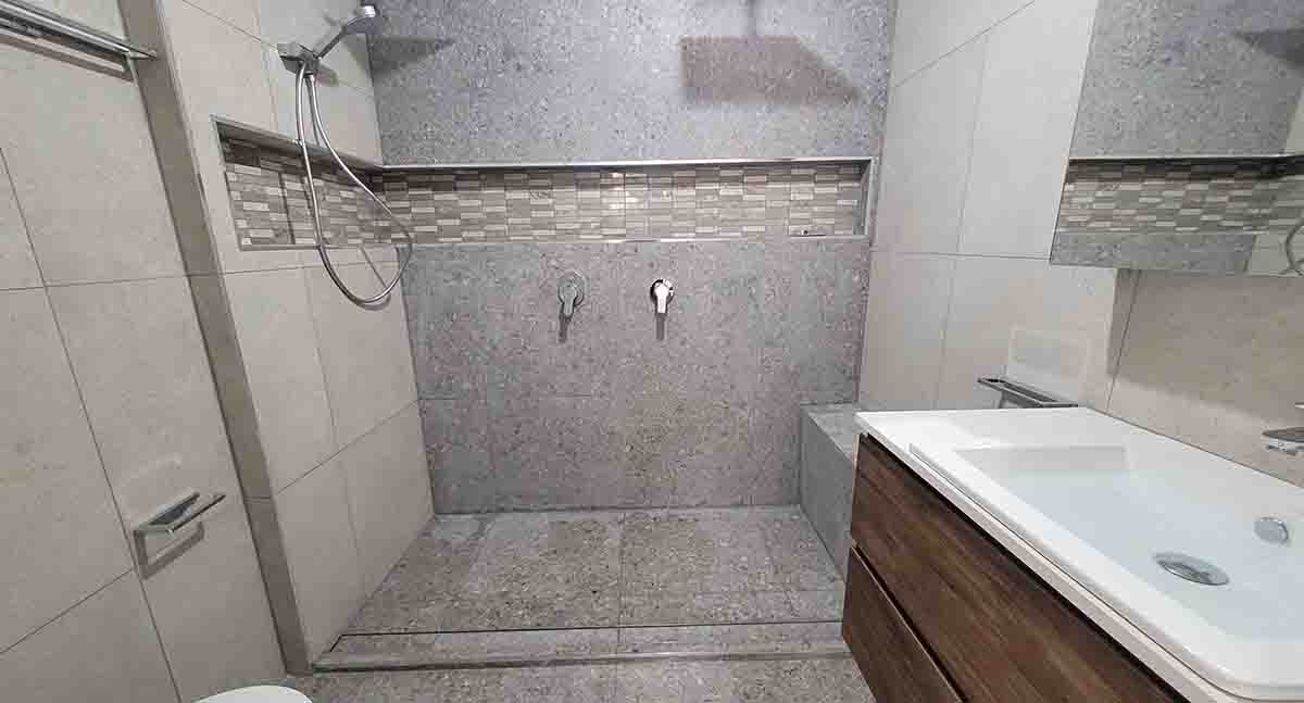 In shower with grey tiles and glass accents in Cranbourne West bathroom renovation.