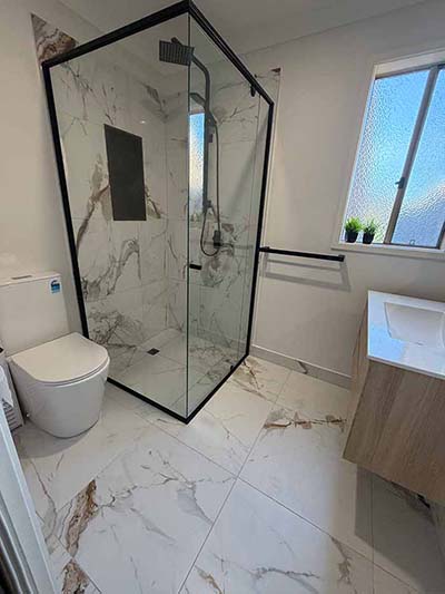 Modern glass shower enclosure with marble tiles in a bathroom.