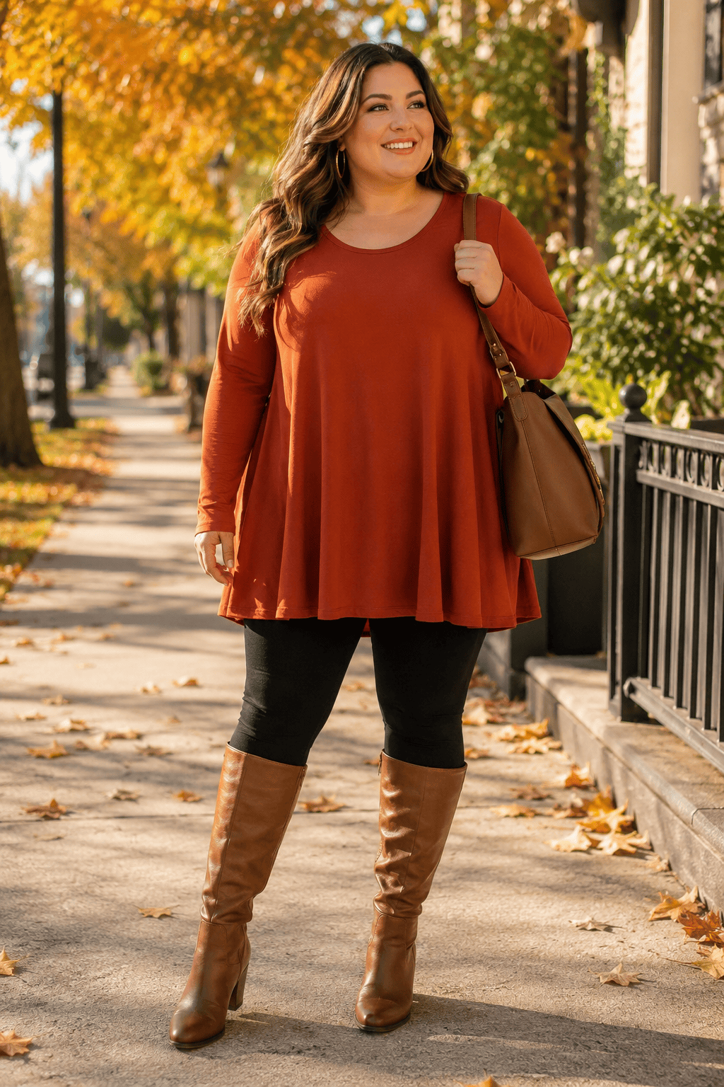 Plus size woman in fall outfit with boots and bag on city sidewalk.
