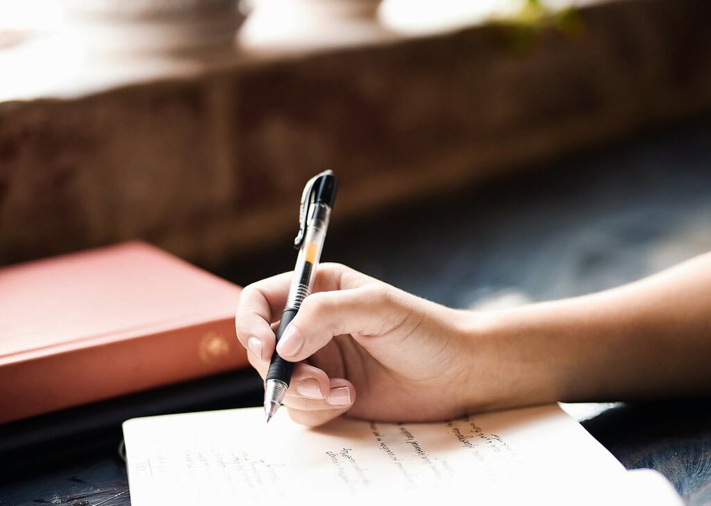 Persona escribiendo en un cuaderno con bolígrafo en un ambiente cálido.