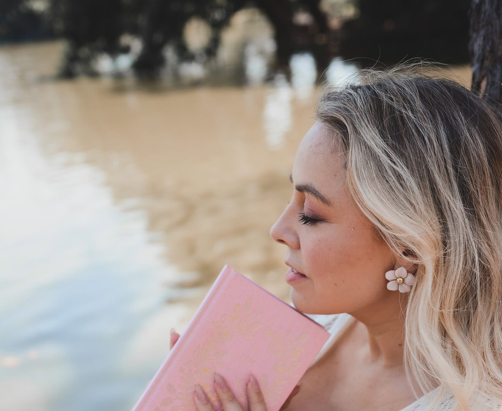 Mujer con libro en la orilla del río, disfrutando de un momento de paz y tranquilidad.