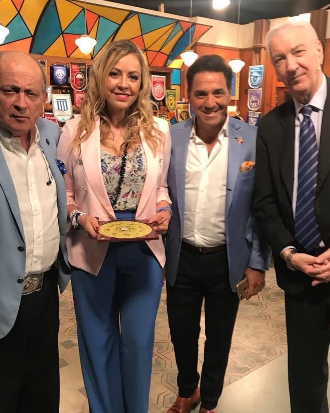 Grupo de cuatro personas en evento con decoraciones coloridas y banderas en el fondo.