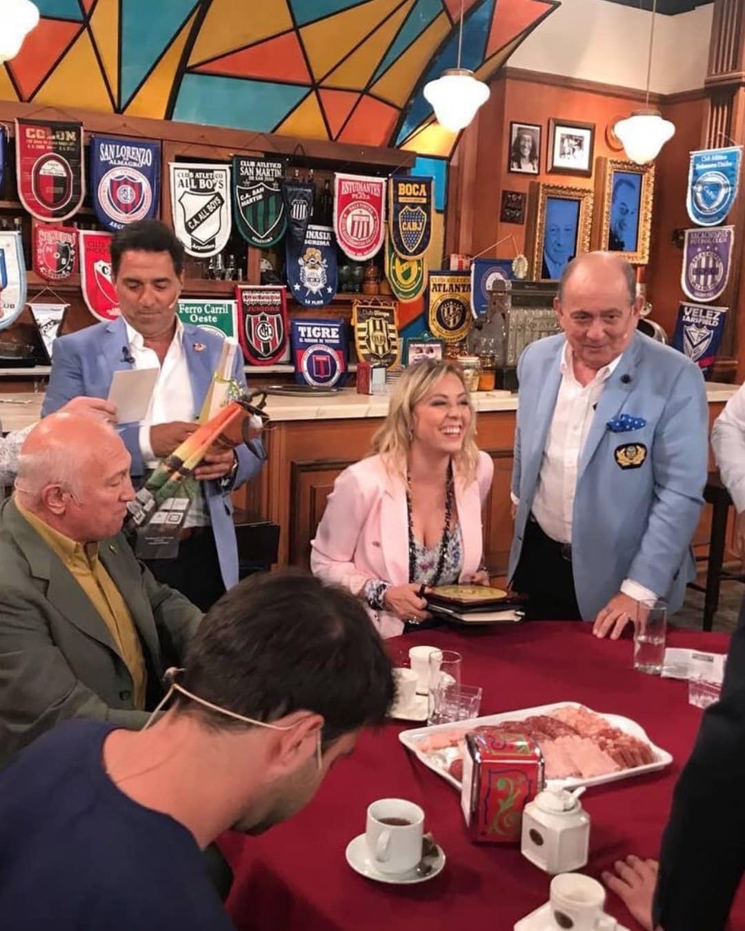 Grupo de personas en reunión social en un bar con banderas y decoraciones coloridas.