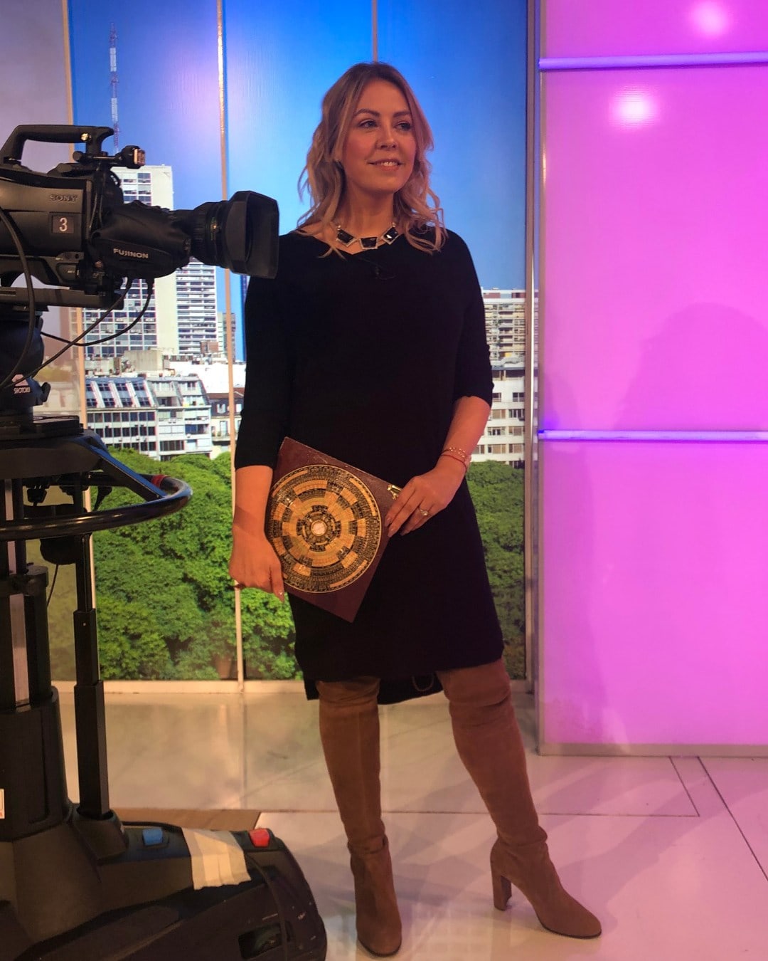Mujer en estudio de televisión con fondo urbano y luces moradas.