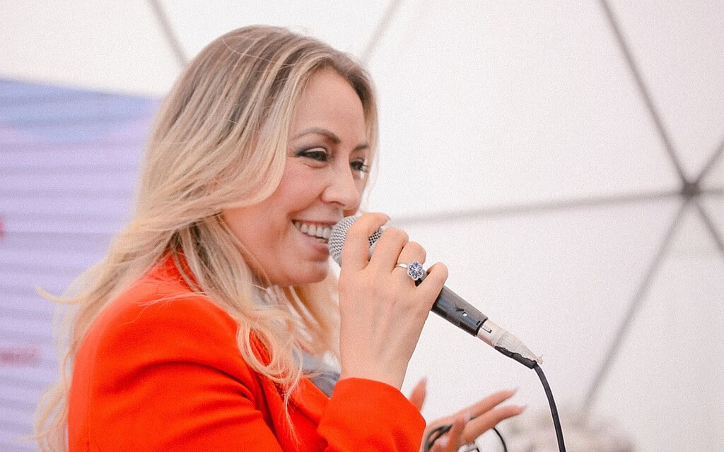 Mujer sonriendo con micrófono en mano, en evento o conferencia.