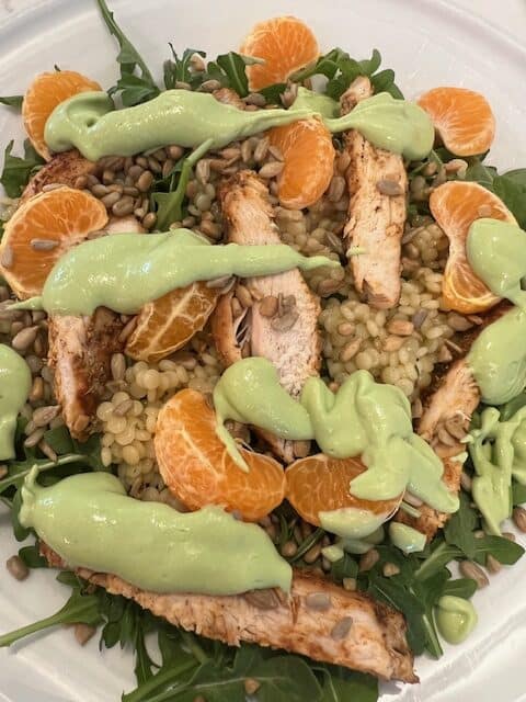 Picture of Arugula Couscous Mandarin Chicken Salad on a white plate drizzled with Lemon Basil Greek Yogurt Dressing.