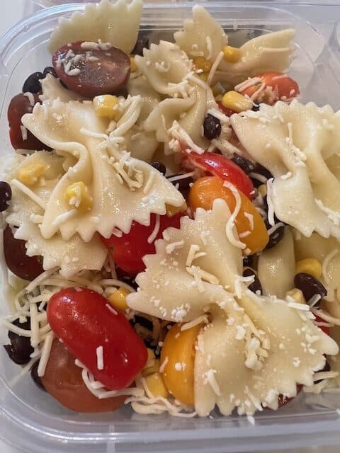 Picture of a lunch container filled with Kids Fiesta Pasta (Bow tie pasta, black beans, corn, Mexican cheese, and cherry tomatoes).