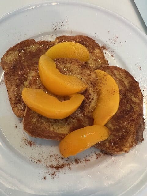 Picture of golden French Toast topped with syrupy peaches and sprinkled with cinnamon.