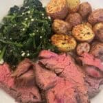 Picture of marinated flank steak on a plate paired with crispy baby potatoes and garlic spinach.