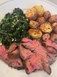 Picture of marinated flank steak on a plate paired with crispy baby potatoes and garlic spinach.