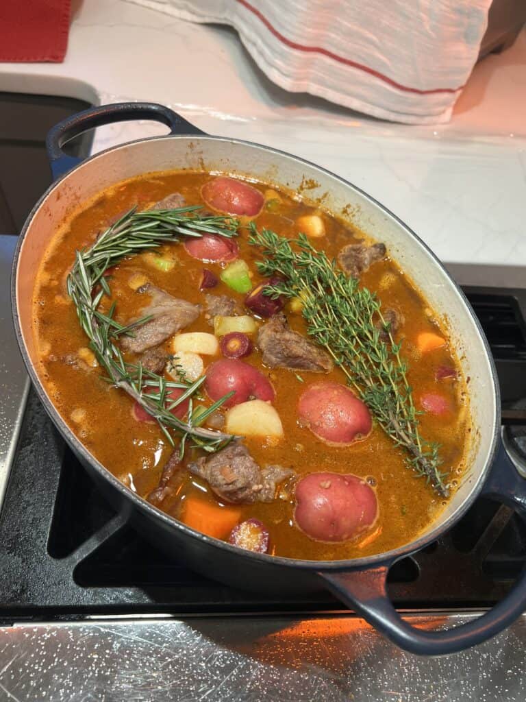 Picture of beef stew cooking on the stove in a pot topped with rosemary.