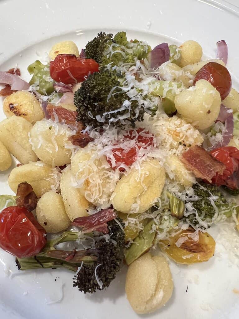 Picture of sheet pan gnocchi on a plate mixed with grilled broccoli, cherry tomatoes, garlic and onion.