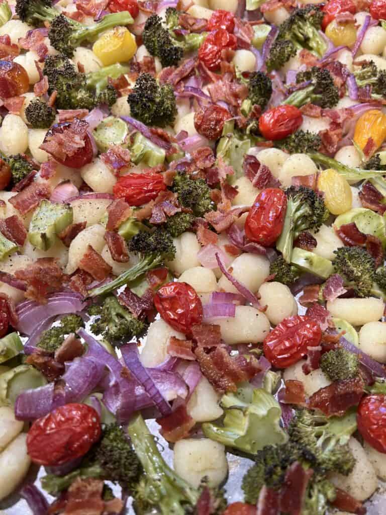 Picture of sheet pan gnocchi on a pan mixed with grilled broccoli, cherry tomatoes, garlic and onion.