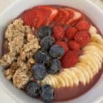 Picture of a simple smoothie bowl topped with fresh strawberries, raspberries, blueberries, sliced banana, and crunchy granola.
