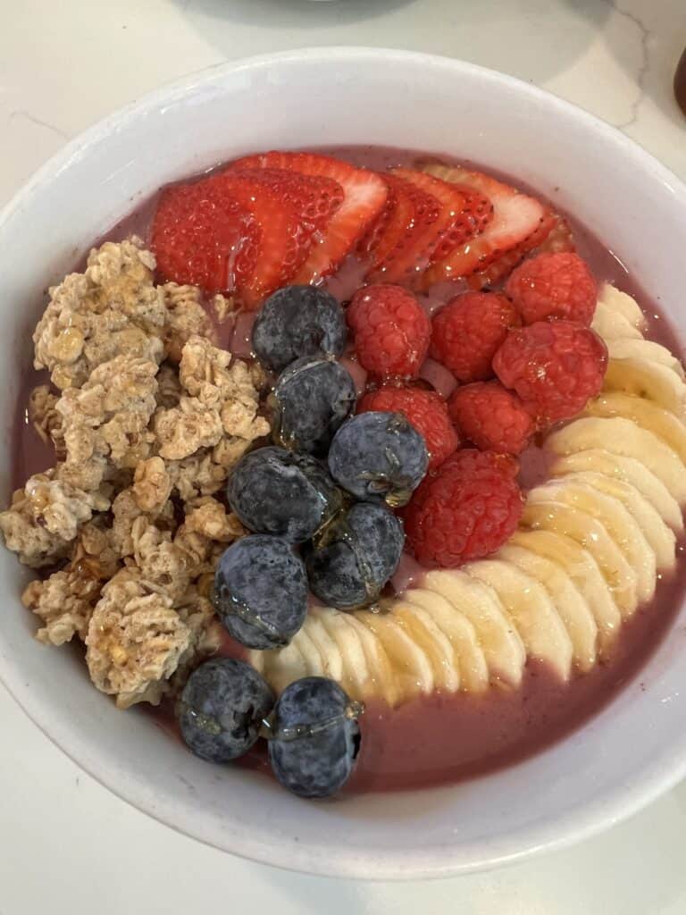 Picture of a simple smoothie bowl topped with fresh strawberries, raspberries, blueberries, sliced banana, and crunchy granola.