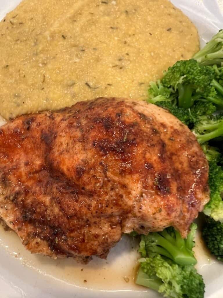 picture of sweet and savory chicken breast plated with creamy polenta and broccoli.